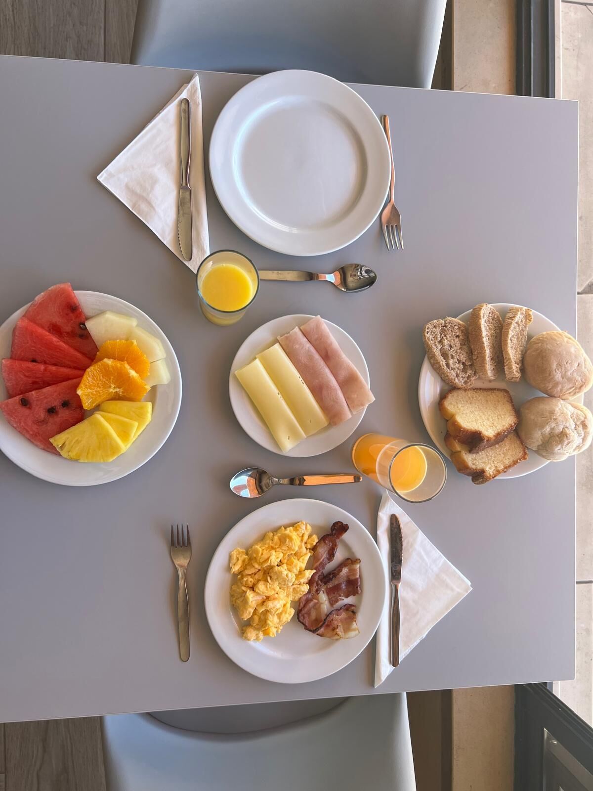 A breakfast table with plates of eggs, bacon, toast, fruit, and juice.