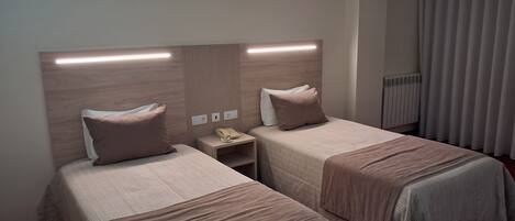 A hotel room with two beds, a bedside table with a telephone, and a radiator.
