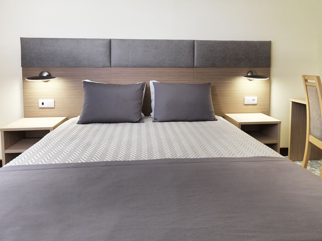 A modern hotel room with a large bed, two bedside tables, and a headboard with integrated lighting.