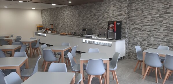 Un café moderno con mostrador, máquinas de café y zona de estar.
