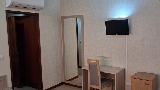 Une pièce comprenant une armoire en bois, un bureau avec une chaise, un miroir et un téléviseur fixé au mur.