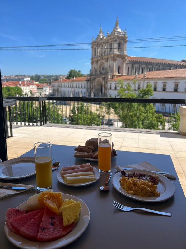 A table with breakfast items and a glass of orange juice, overlooking a historic building.