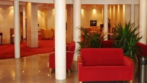 A lobby with red sofas, white pillars, and a red carpet. - Hotel Santa Maria (Alcobaça)
