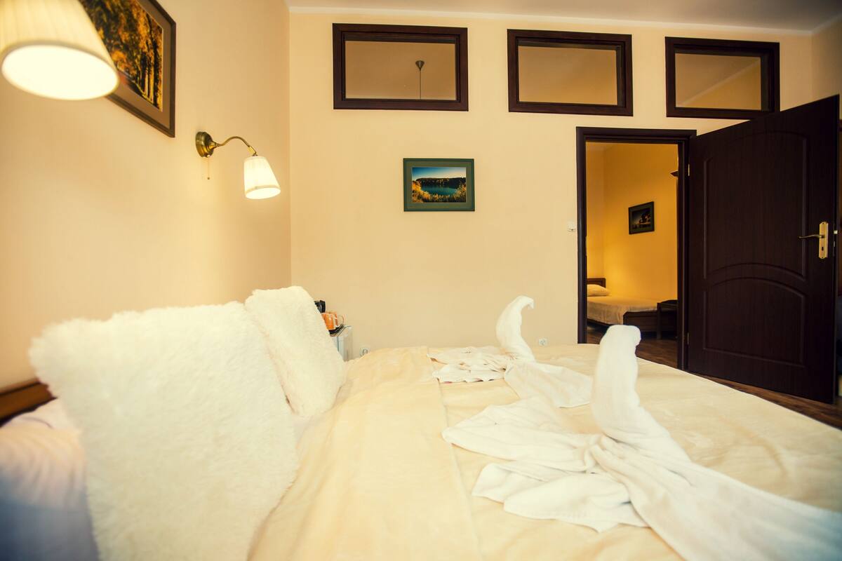 Een hotelkamer met een bed, een nachtkastje, een ingelijst beeld en een deur die naar een andere kamer leidt.