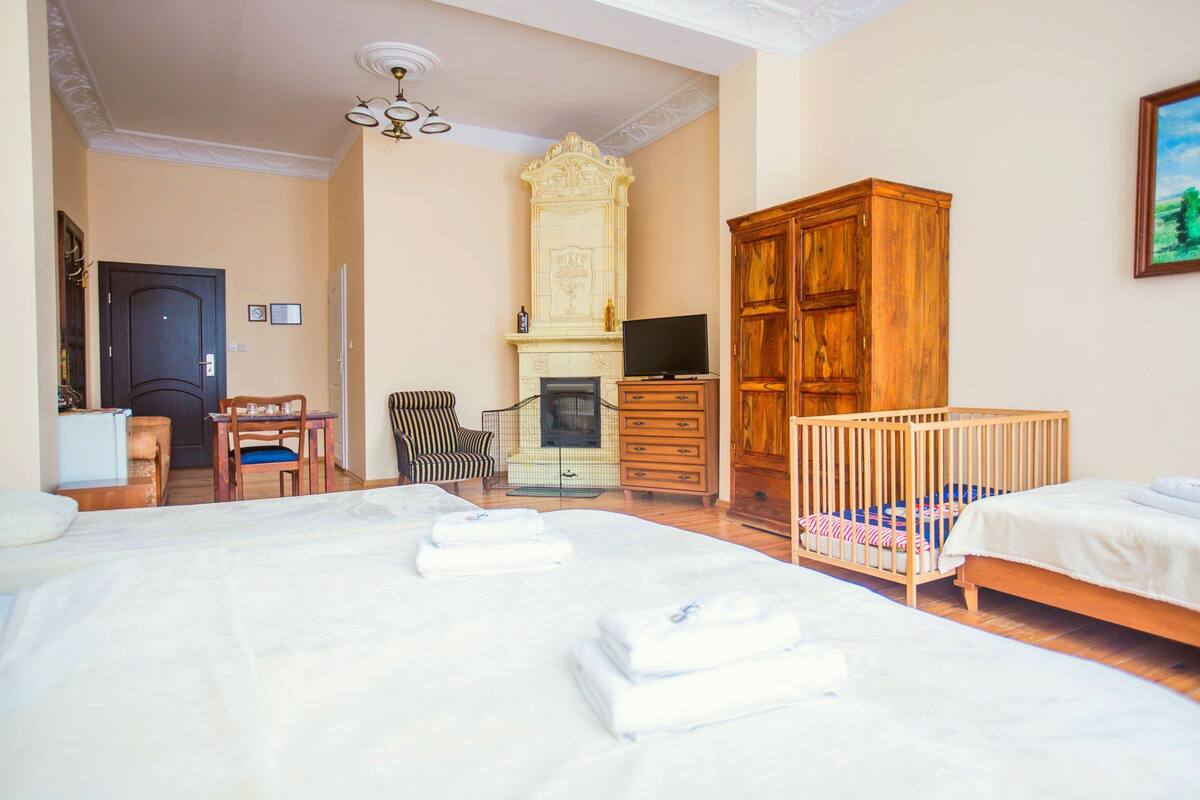 Hotelkamer met een bed, een reisbedje, een houten garderobe, een televisie, een open haard, en een zithoek met een stoel en tafel.
