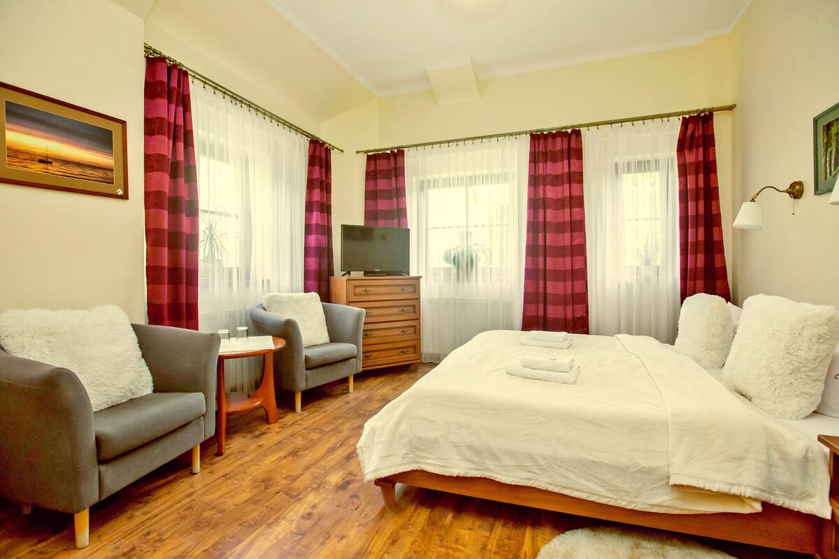 Een slaapkamer met een groot bed, een bank, een stoel, een televisie en een dressoir.