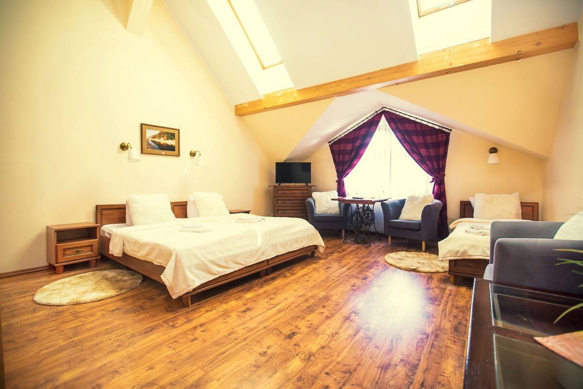 Een gezellige slaapkamer met een houten vloer, een bed, een sofa, een televisie en een kleine tafel.