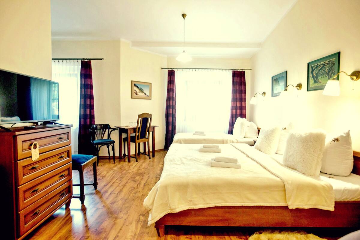 Een hotelkamer met een houten dressoir, een bureau, twee bedden en een raam met gordijnen.