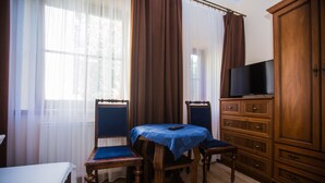 A hotel room with a bed, a wooden table with a blue tablecloth, two chairs, a television on a wooden cabinet, and a large window with curtains. - Pod Kasztanami (Swinoujscie)