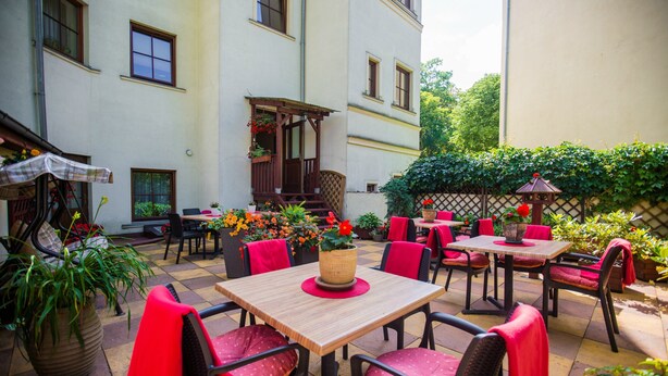 An outdoor patio with tables and chairs, surrounded by plants and a wooden pergola. - Pod Kasztanami (Swinoujscie)