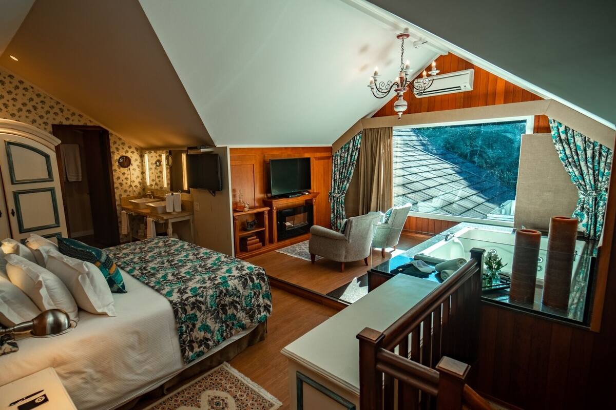 A bedroom with a large bed, a sitting area with a TV, and a balcony with a view.