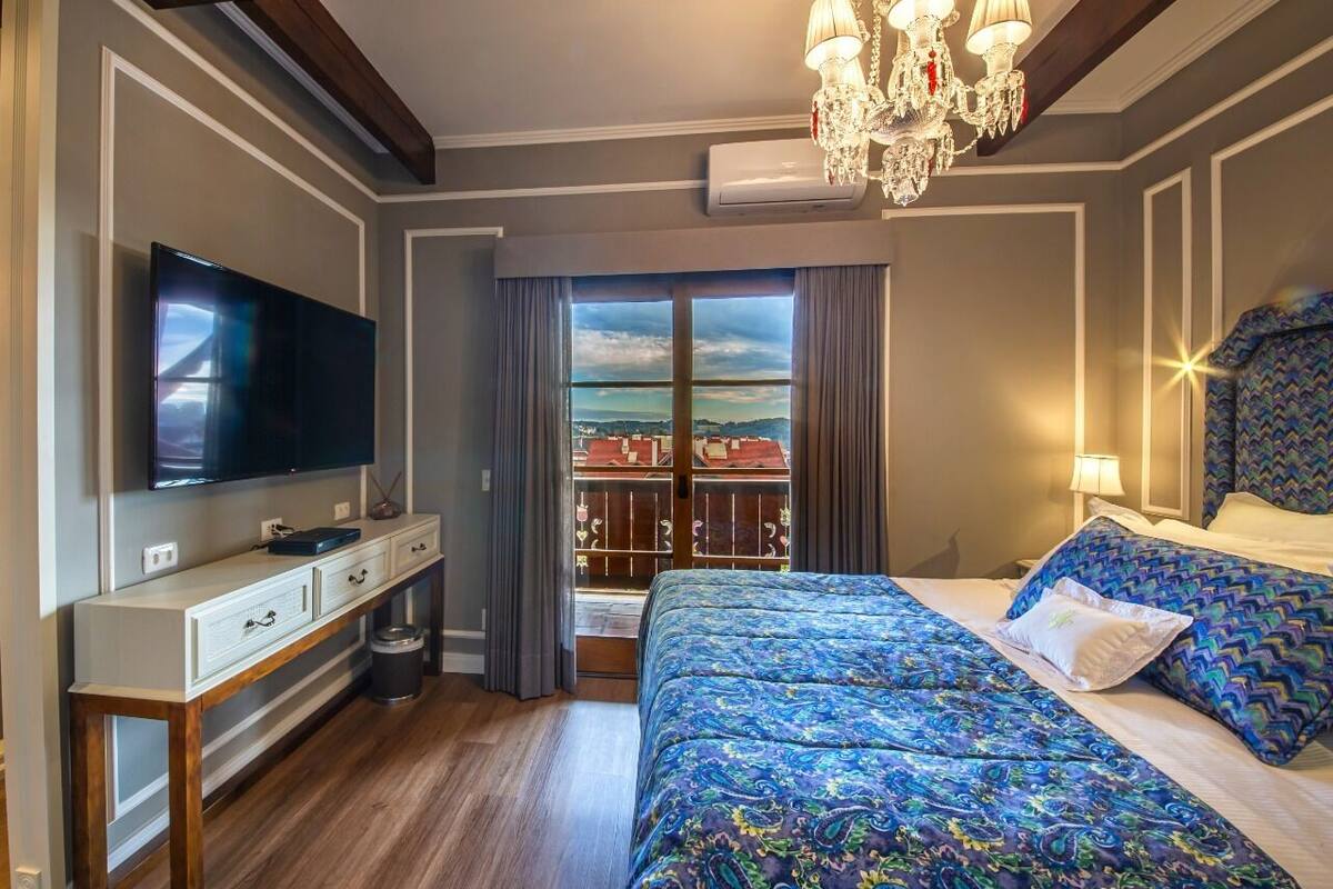 A hotel room with a large bed, a TV, a desk, and a balcony with a view.