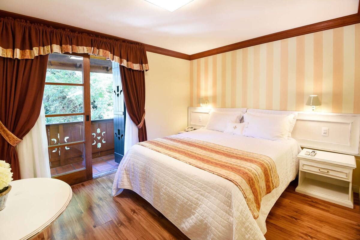 A bedroom with a large bed, a nightstand, a bedside table, and a window with curtains.