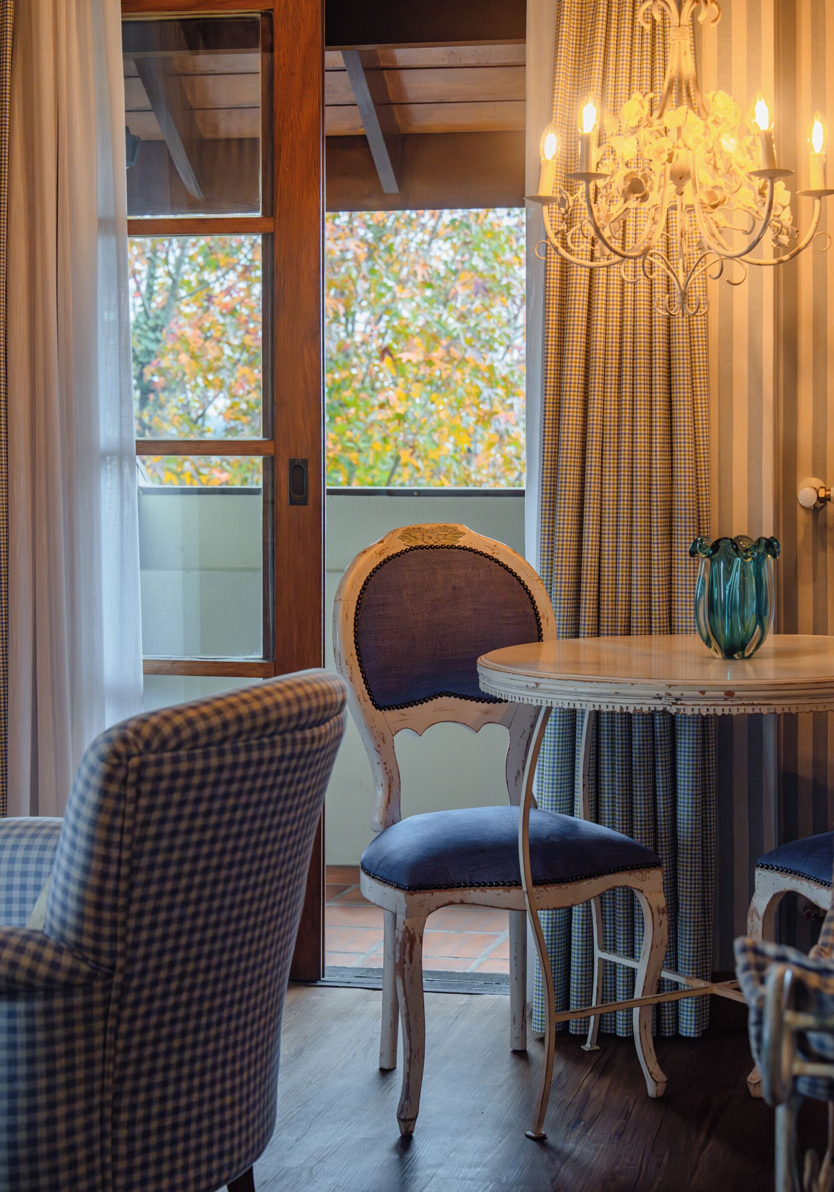 A room with a checkered chair, a round table with a vase, and a chandelier.