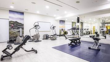 Un gimnasio moderno con varios equipos de ejercicio, un espejo grande y una zona de colchonetas azules.