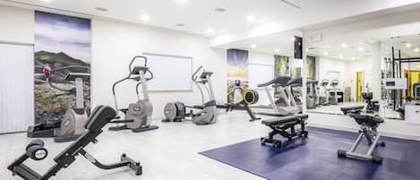 Un gimnasio moderno con varios equipos de ejercicio, un espejo grande y una zona de colchonetas azules.