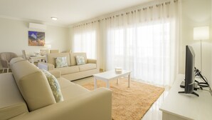 Een moderne woonkamer met een beige bank, een witte salontafel en een flatscreen televisie op een wit bureau.