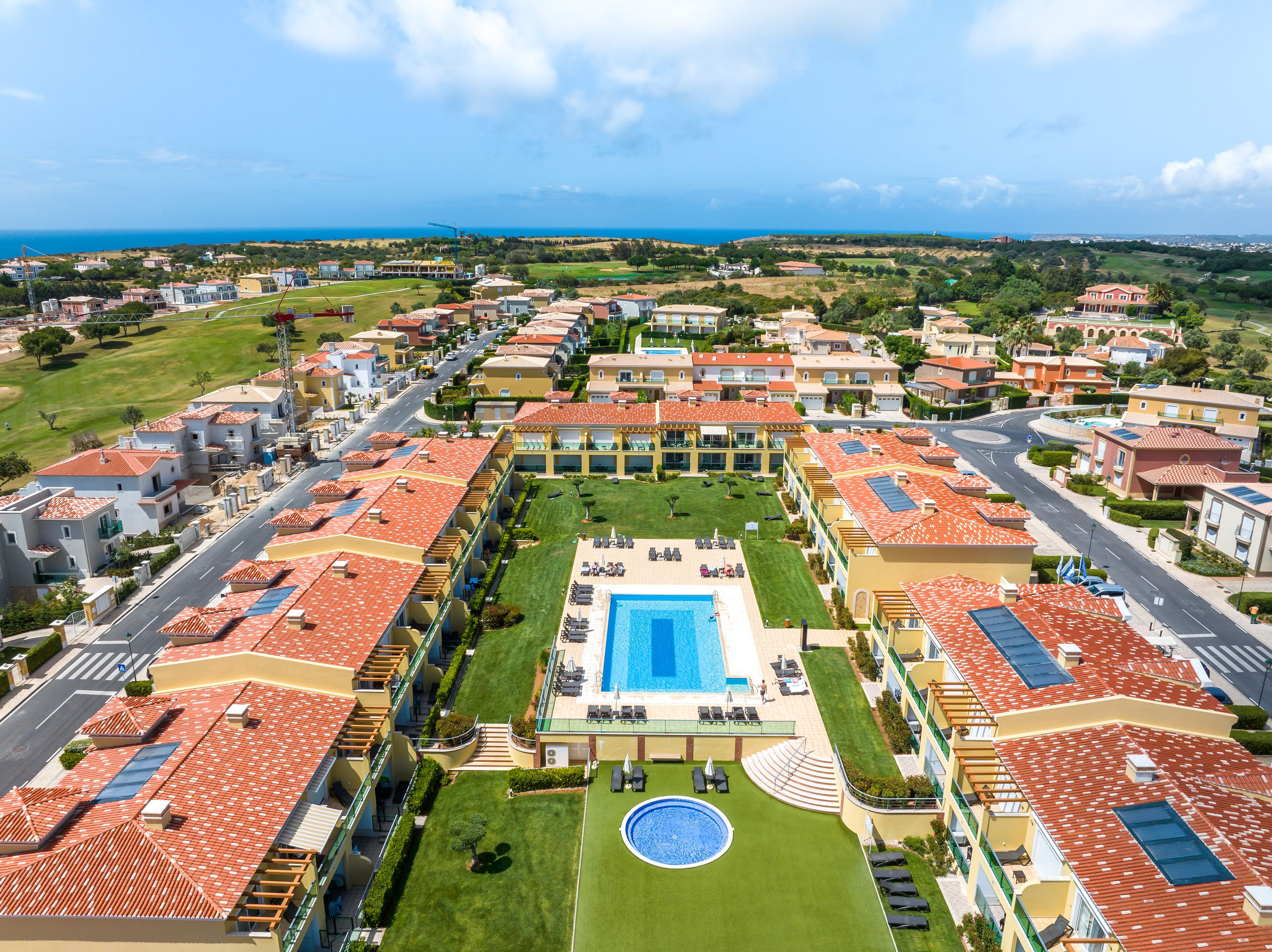 Um resort com piscina central, vários edifícios com telhados de barro vermelho e vista para o mar.