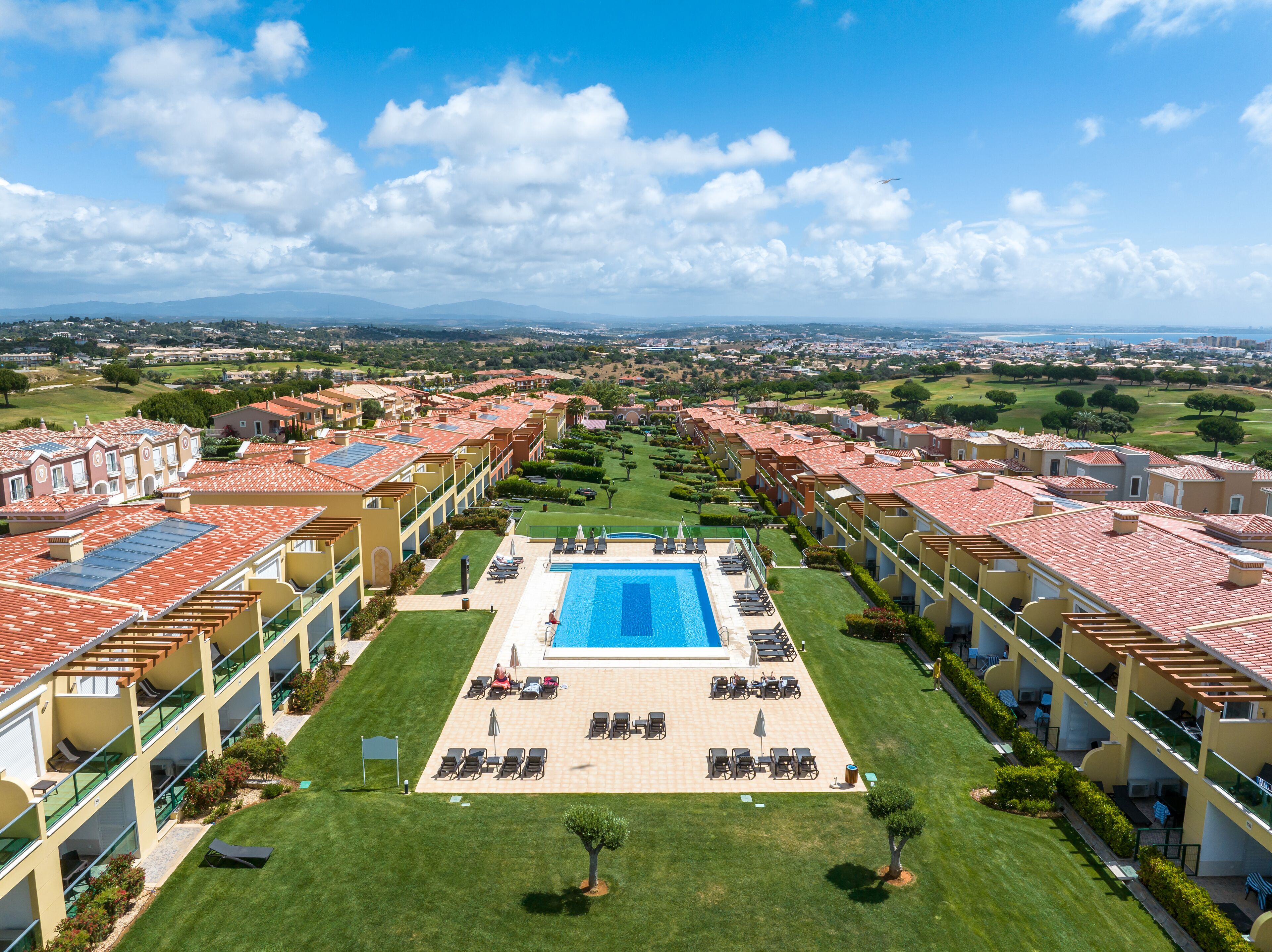 A resort with a central swimming pool, multiple balconies, and a view of the surrounding landscape.