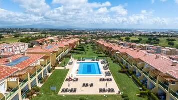 A resort with a central swimming pool, multiple balconies, and a view of the surrounding landscape.
