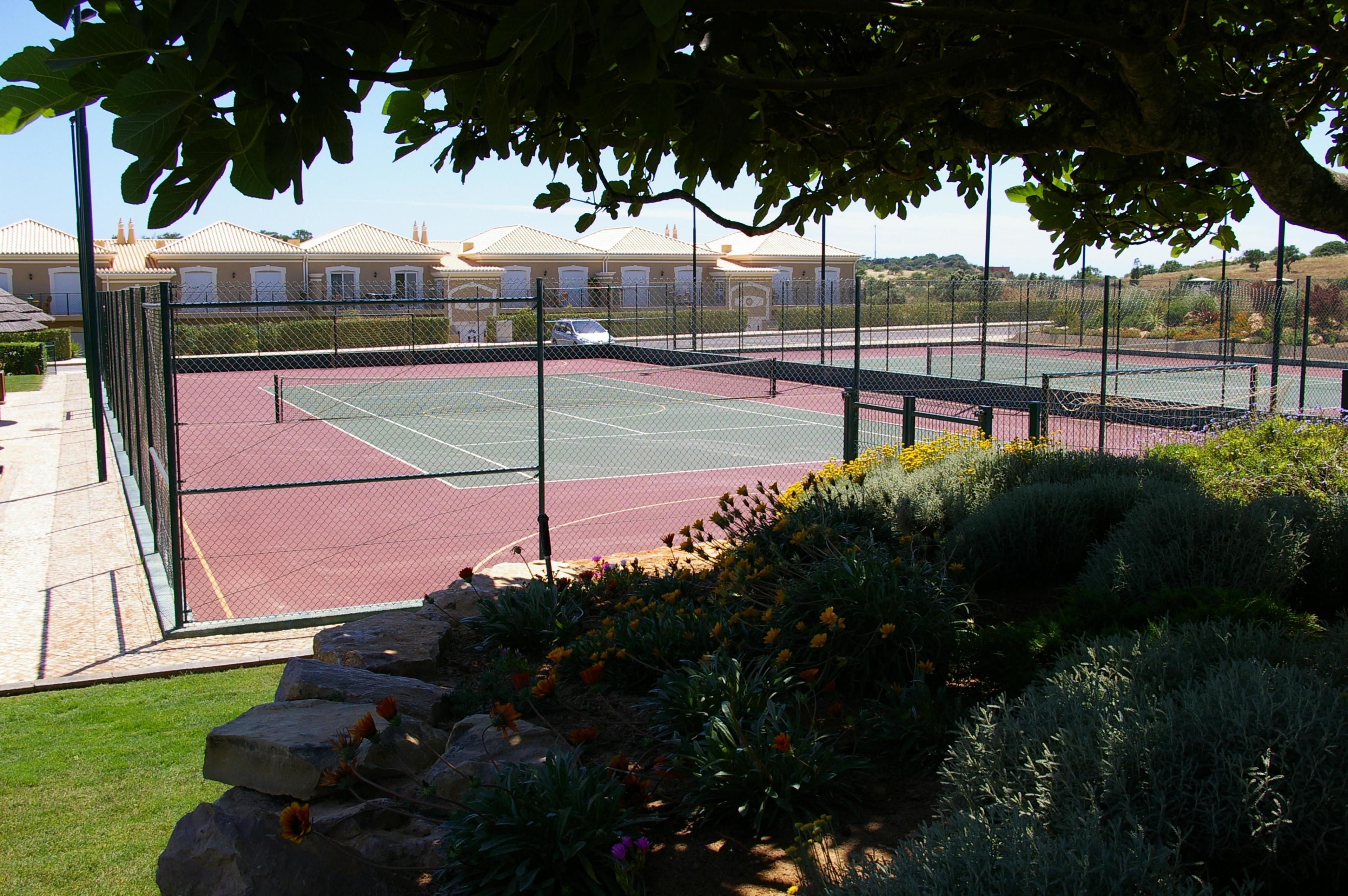 Una cancha de tenis rodeada por una valla, con un edificio al fondo.