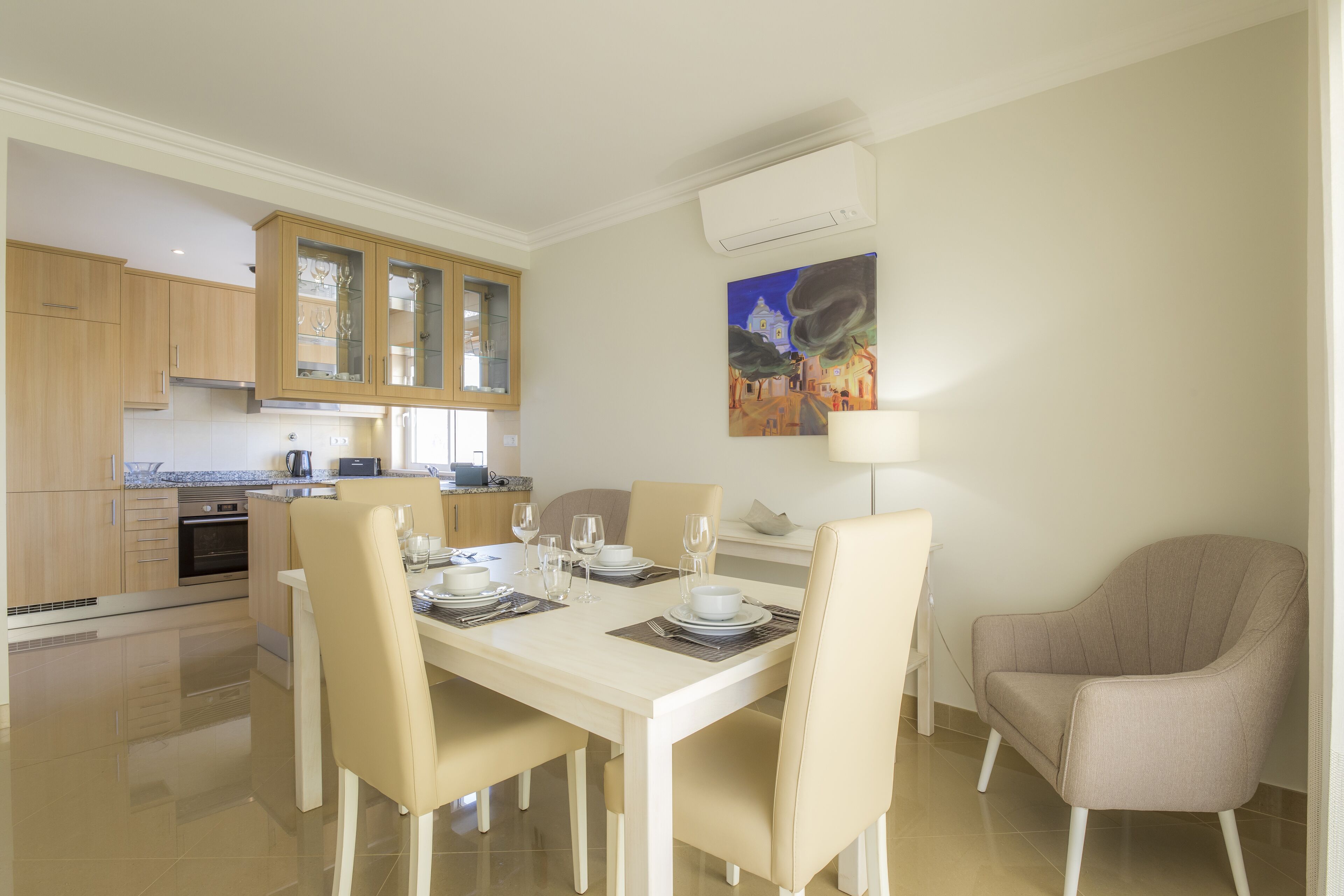 Une cuisine moderne avec des meubles en bois, une table à manger dressée pour quatre personnes et un tableau accroché au mur.