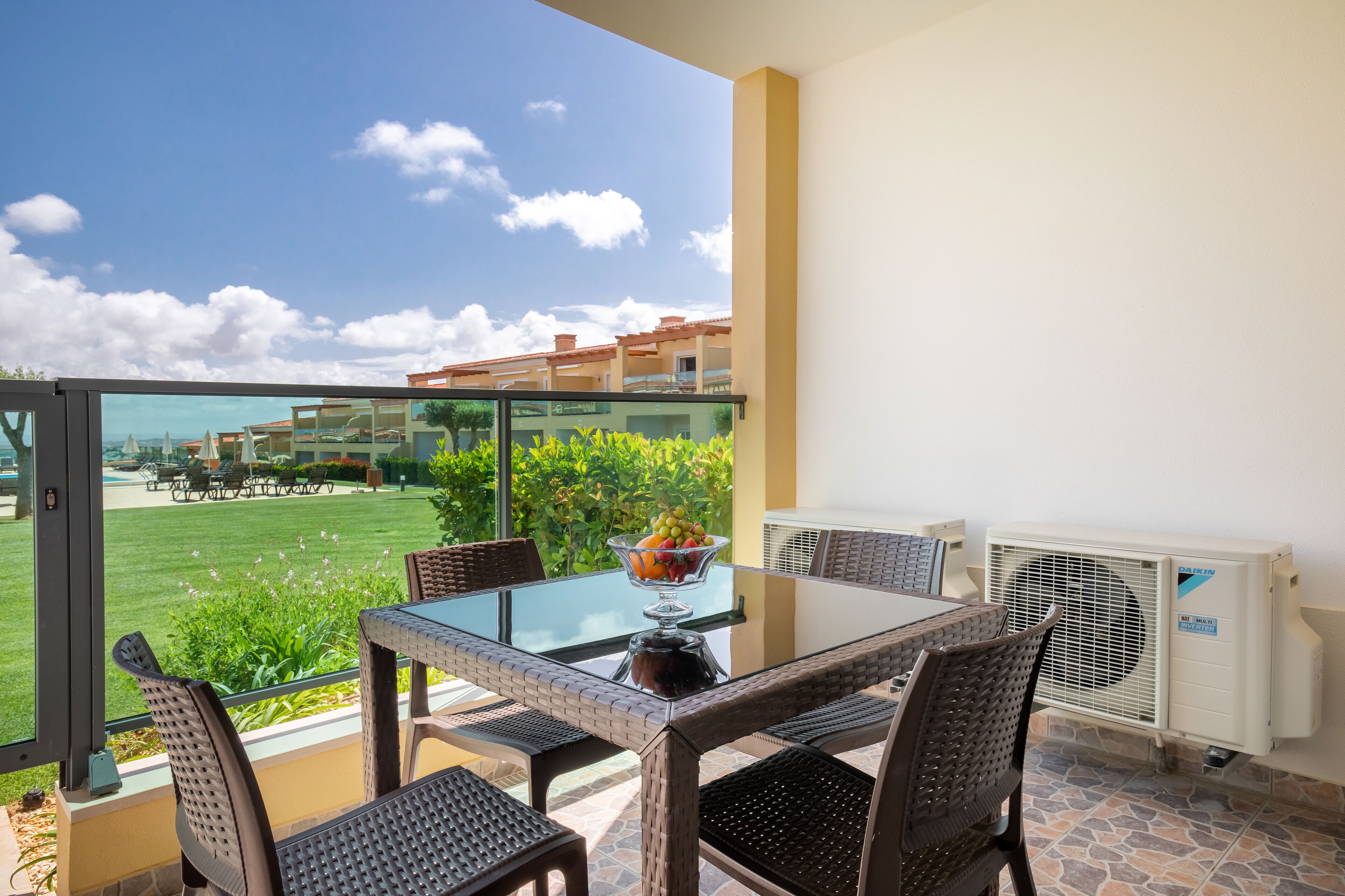 A balcony with a glass table, wicker chairs, and a bowl of fruit.
