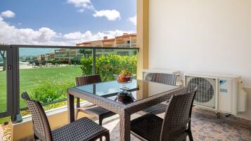 A balcony with a glass table, wicker chairs, and a bowl of fruit.