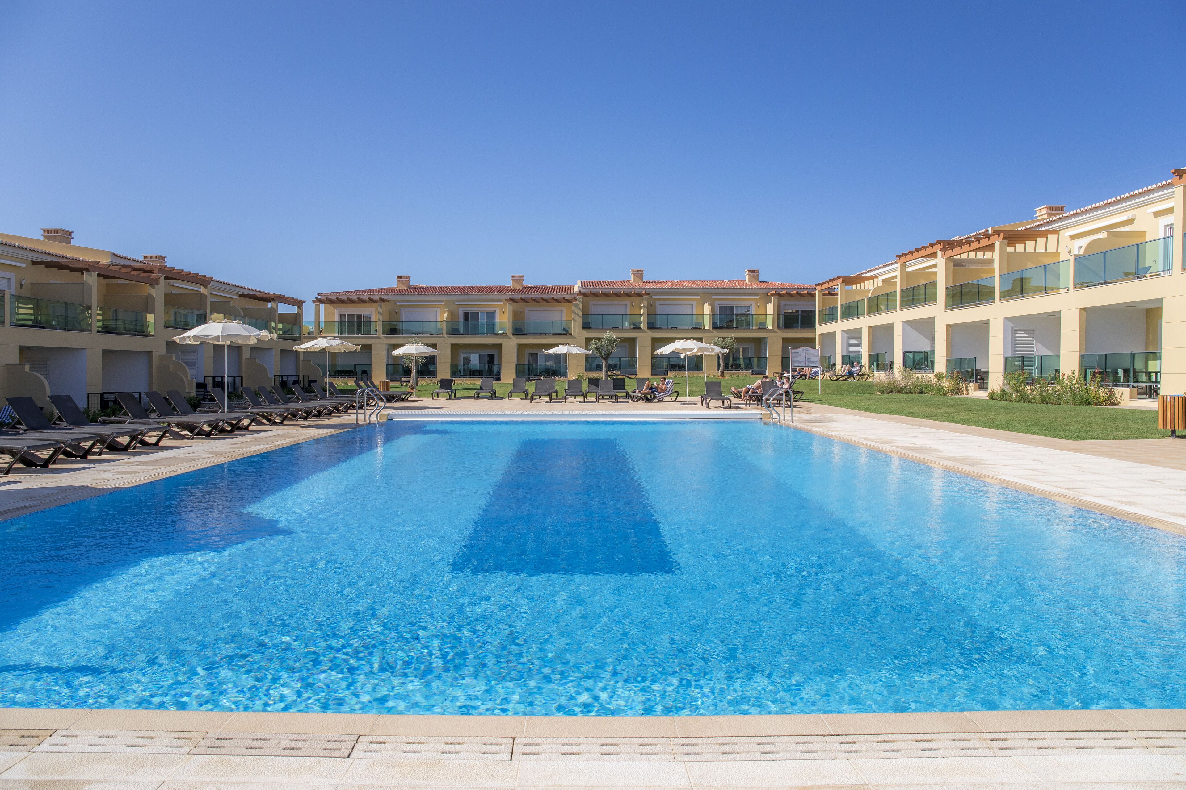 Une grande piscine rectangulaire à l’eau d’un bleu limpide, entourée de chaises longues et de parasols.