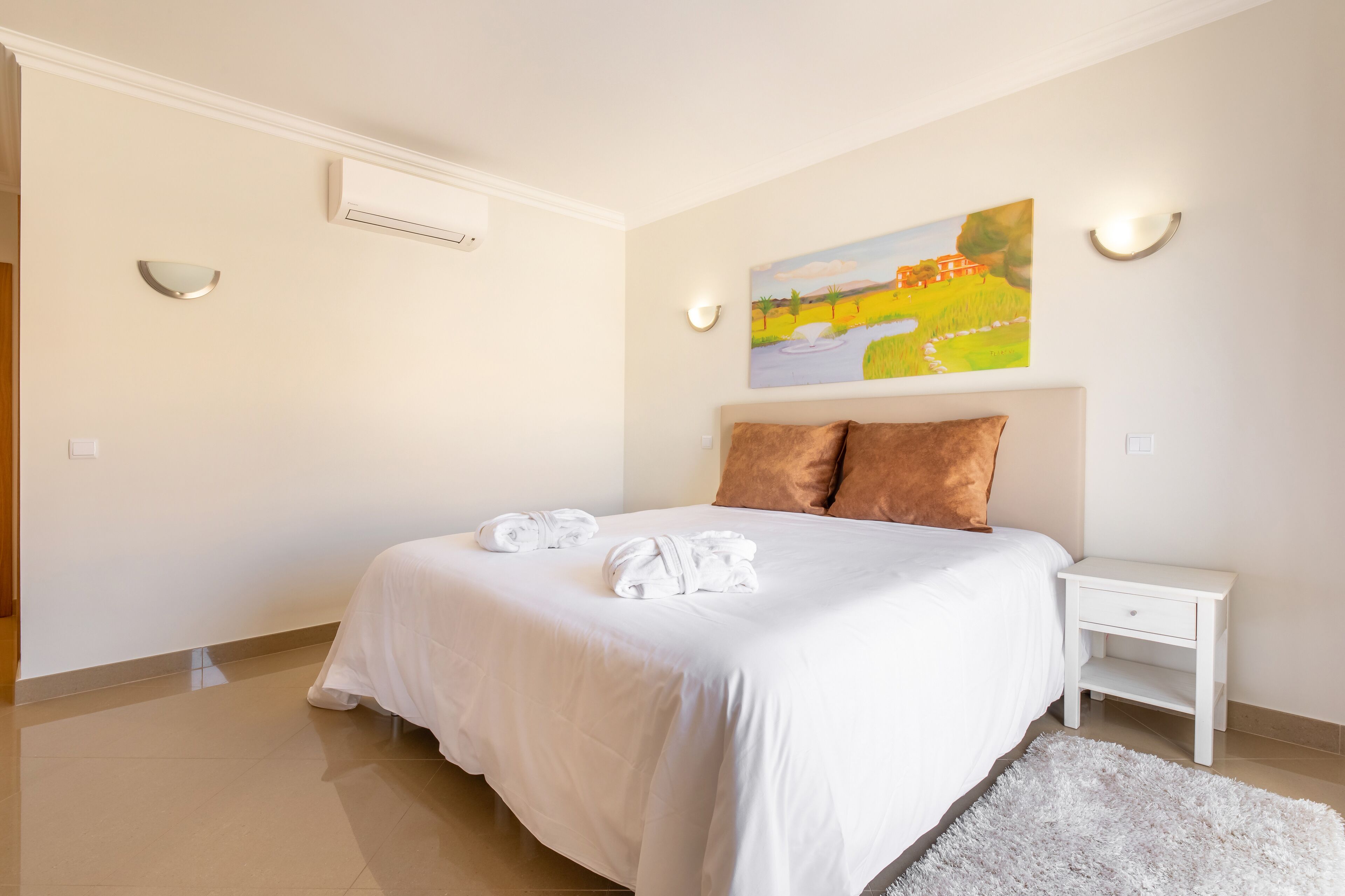 Une chambre à coucher avec un grand lit, du linge de lit blanc, une table de chevet blanche et un tableau au mur.