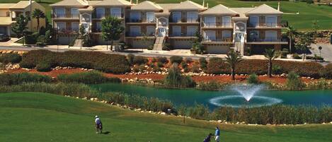 Un campo de golf con un estanque, palmeras y un complejo de edificios al fondo.