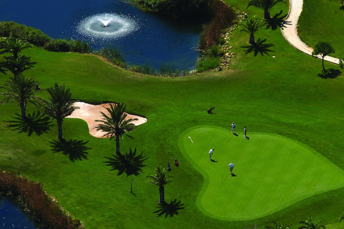 Een golfbaan met een vijver, palmbomen en een fontein.