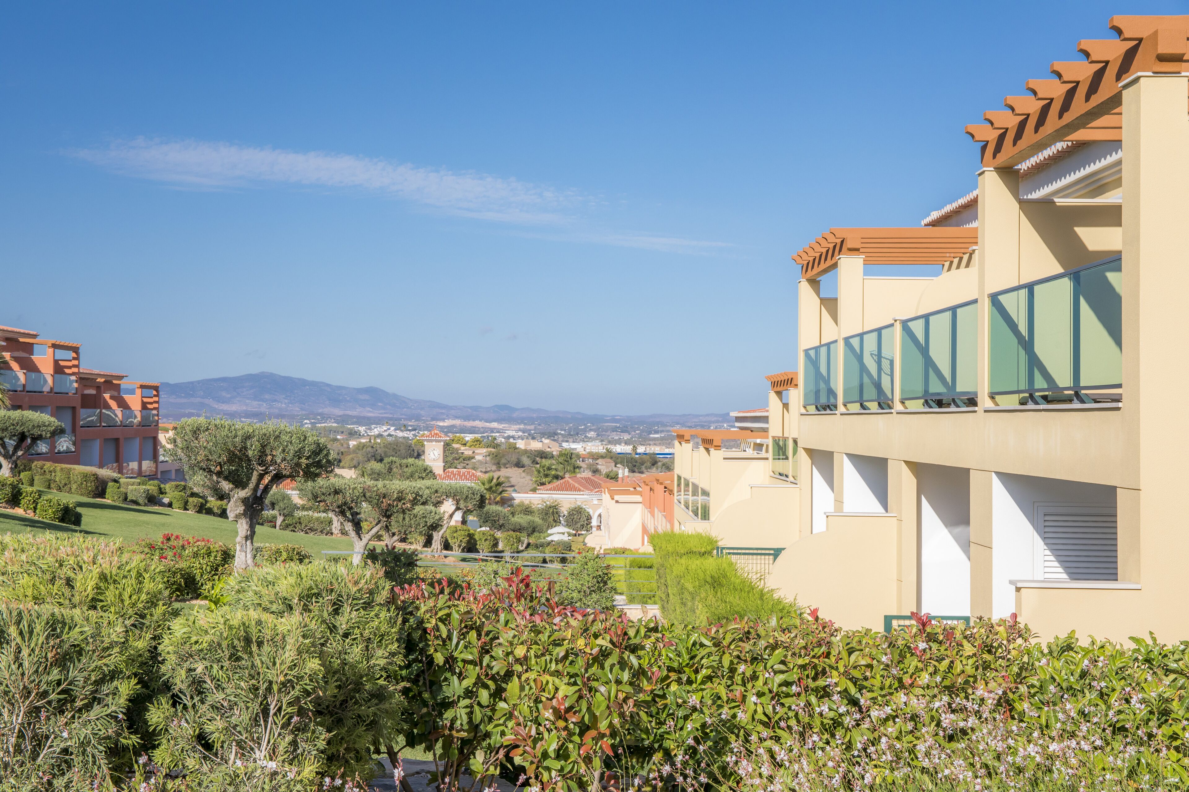 Un bâtiment moderne doté de balcons donnant sur un jardin aménagé et sur des montagnes lointaines.