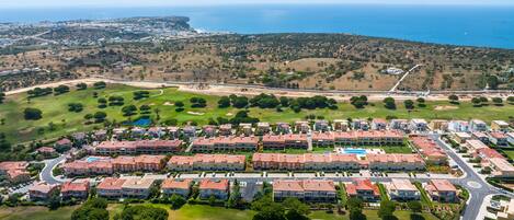 An aerial view of a coastal resort with multiple buildings, a golf course, and a view of the ocean.