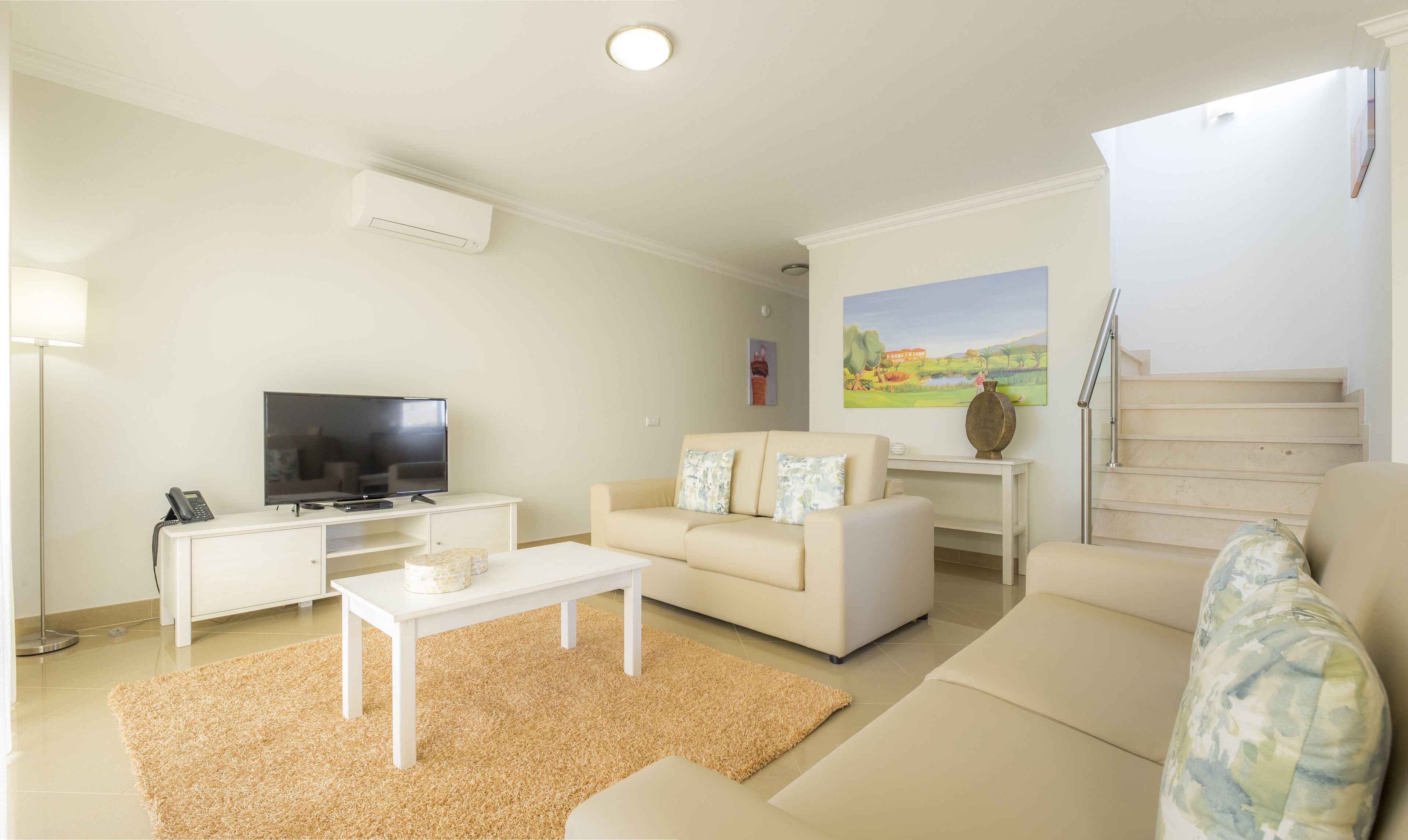 A living room with a sofa, a coffee table, a TV, and a painting on the wall.