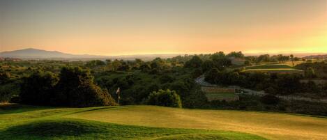 A golf course with rolling hills, trees, and a distant mountain range.