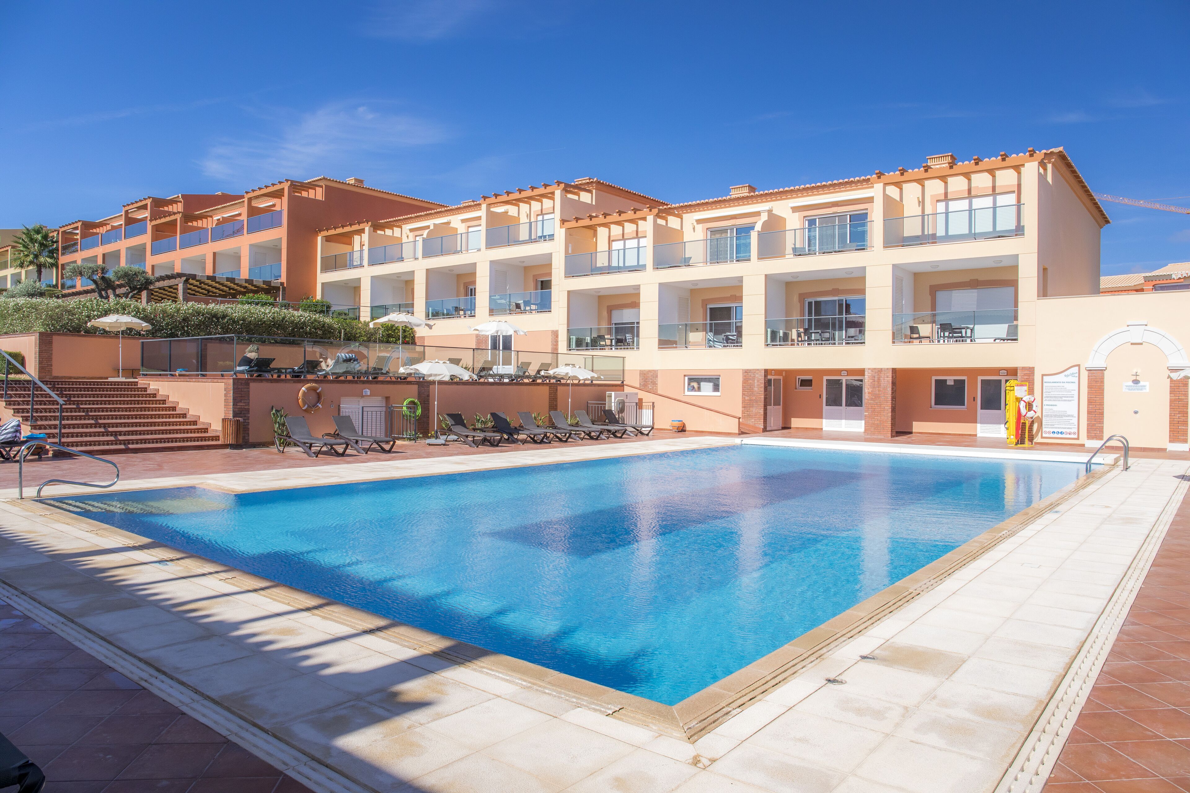 Un hotel con piscina, varios balcones y un cielo azul despejado.