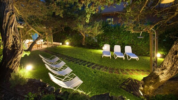 A well-lit outdoor seating area with lounge chairs and a hammock, surrounded by trees and a building in the background. - Hotel Nina (Bibbona)