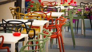 A dining area with multiple tables and chairs, some with colorful frames. - Hotel Nina (Bibbona)