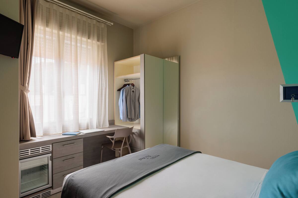 A bedroom with a bed, a desk, a chair, a wardrobe, and a television.