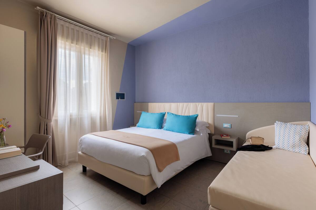 A hotel room with a bed, bedside tables, a desk, and a chair.