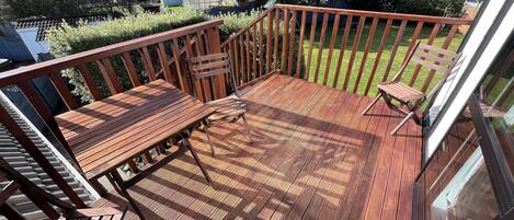 A wooden deck with a table and chairs, overlooking a well-maintained lawn and neighboring houses.
