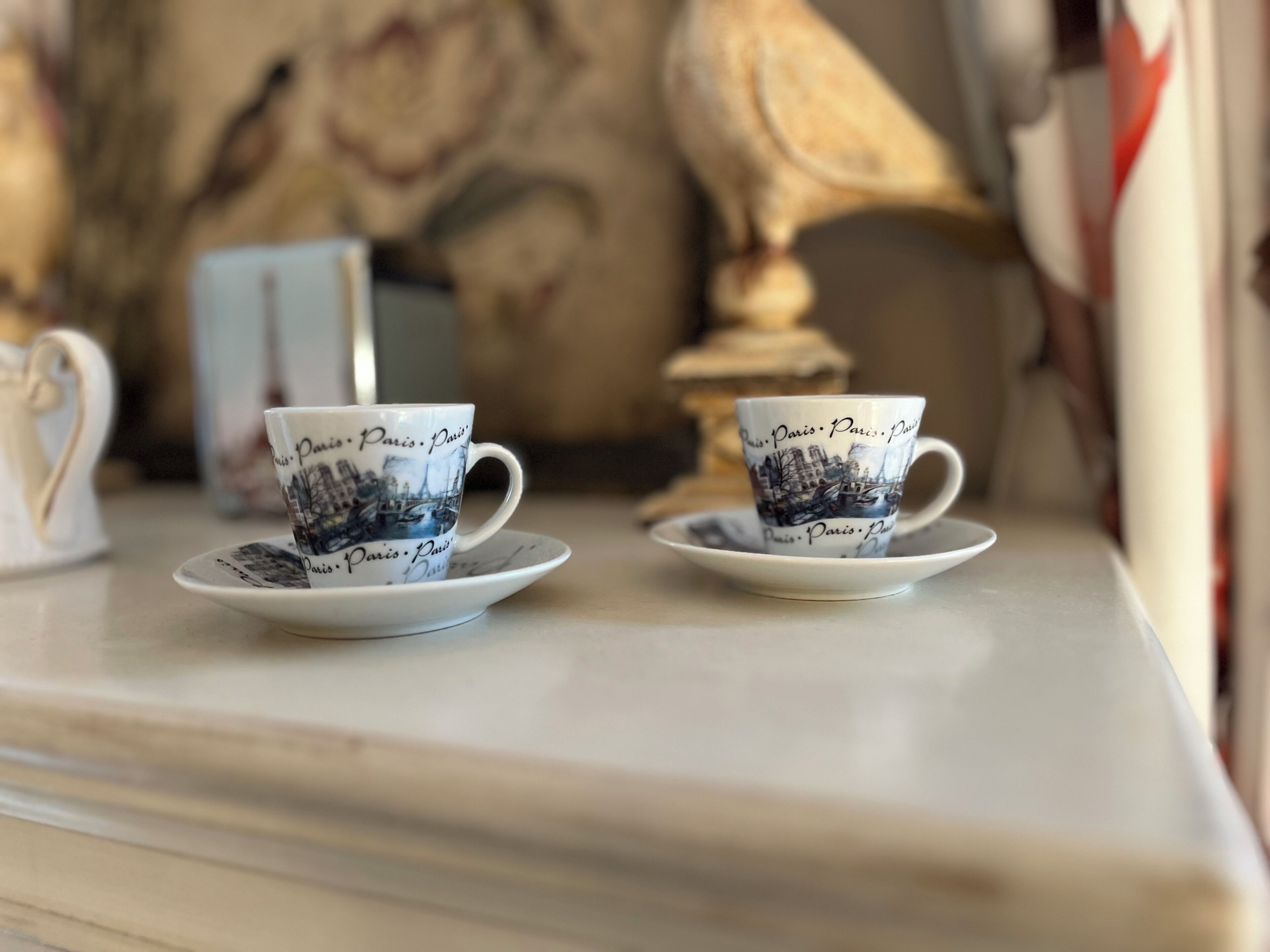 Two cups with 'Paris' text on them, placed on saucers on a table.