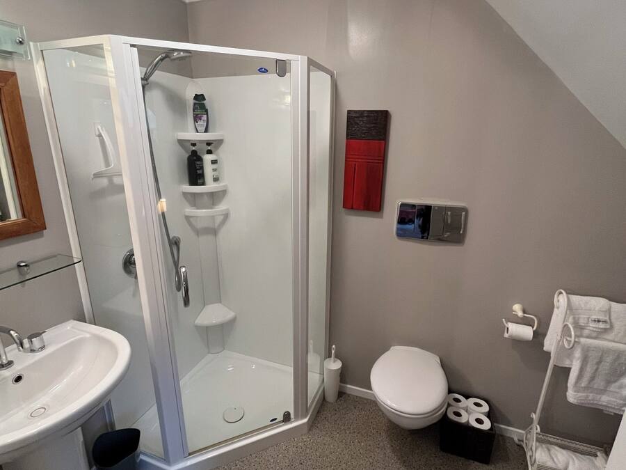 Un baño moderno con ducha de vidrio, lavamanos blanco, inodoro y toallero.