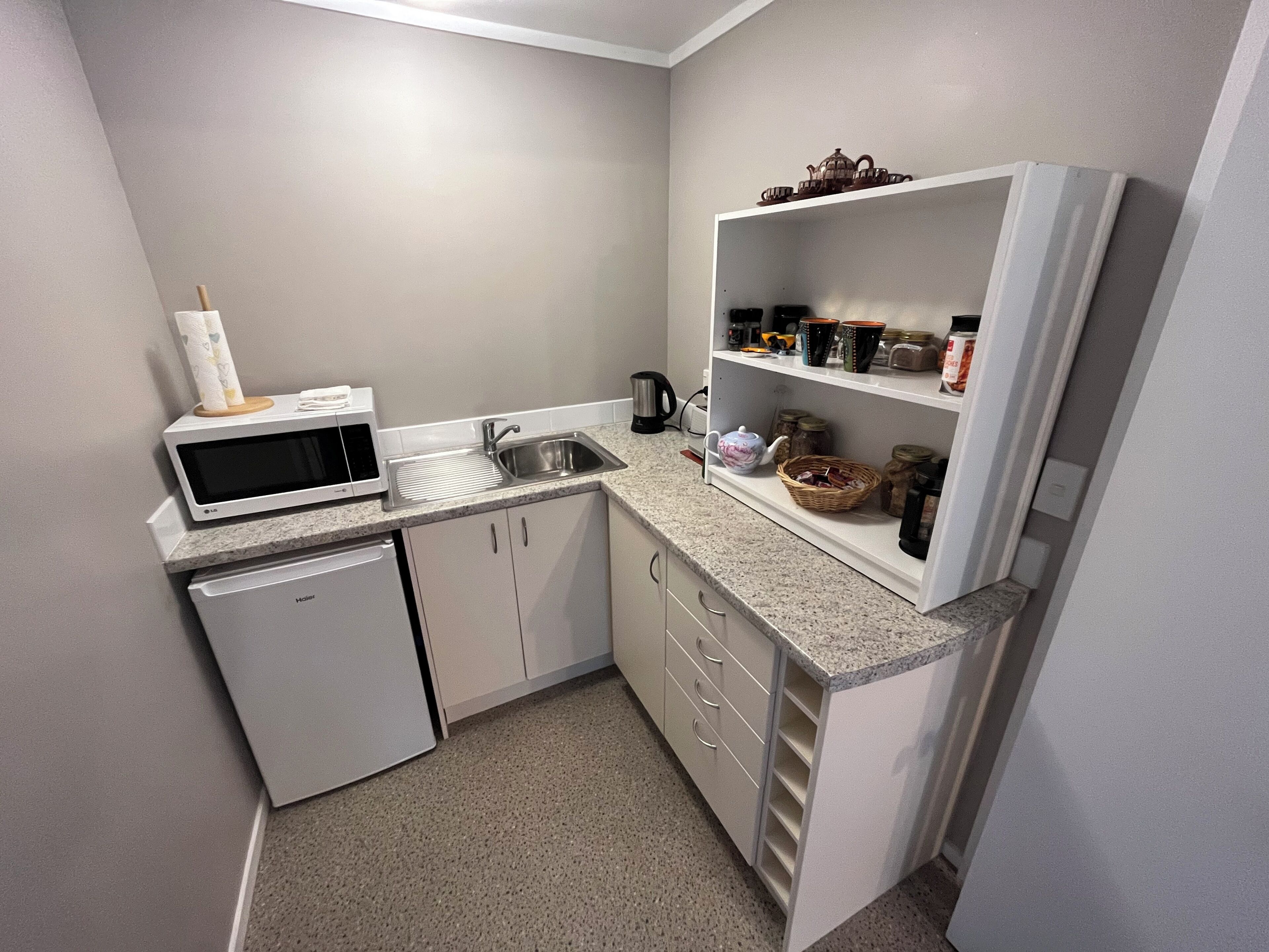A compact kitchen with a microwave, sink, and white cabinets.