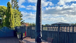 An outdoor patio with a table and chairs, a covered grill, and a wooden fence. - Tudor Manor Bed & Breakfast (Paraparaumu)