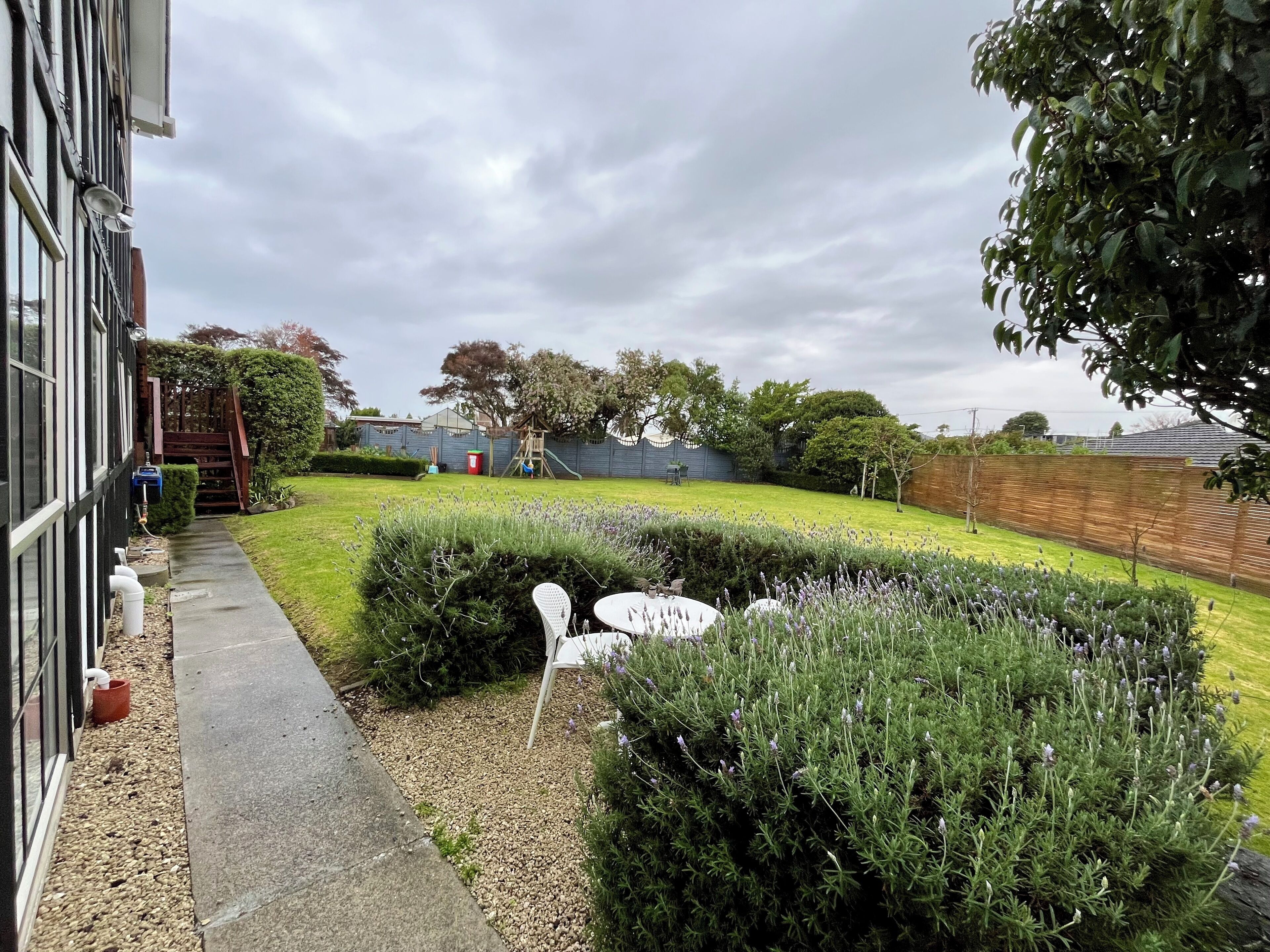 A residential backyard with a paved pathway, neatly trimmed hedges, and a play area.