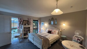 A bedroom with a bed, bedside table, and a small table with an ironing board. - Tudor Manor Bed & Breakfast (Paraparaumu)