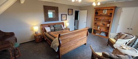 A spacious bedroom with a large wooden bed, a wicker chair, and a small round table.
