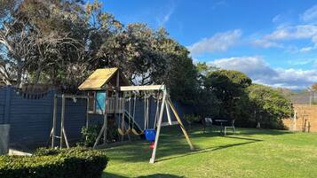 Enjoy outdoor dining or relaxation in this serene backyard with a charming playhouse and lush greenery.